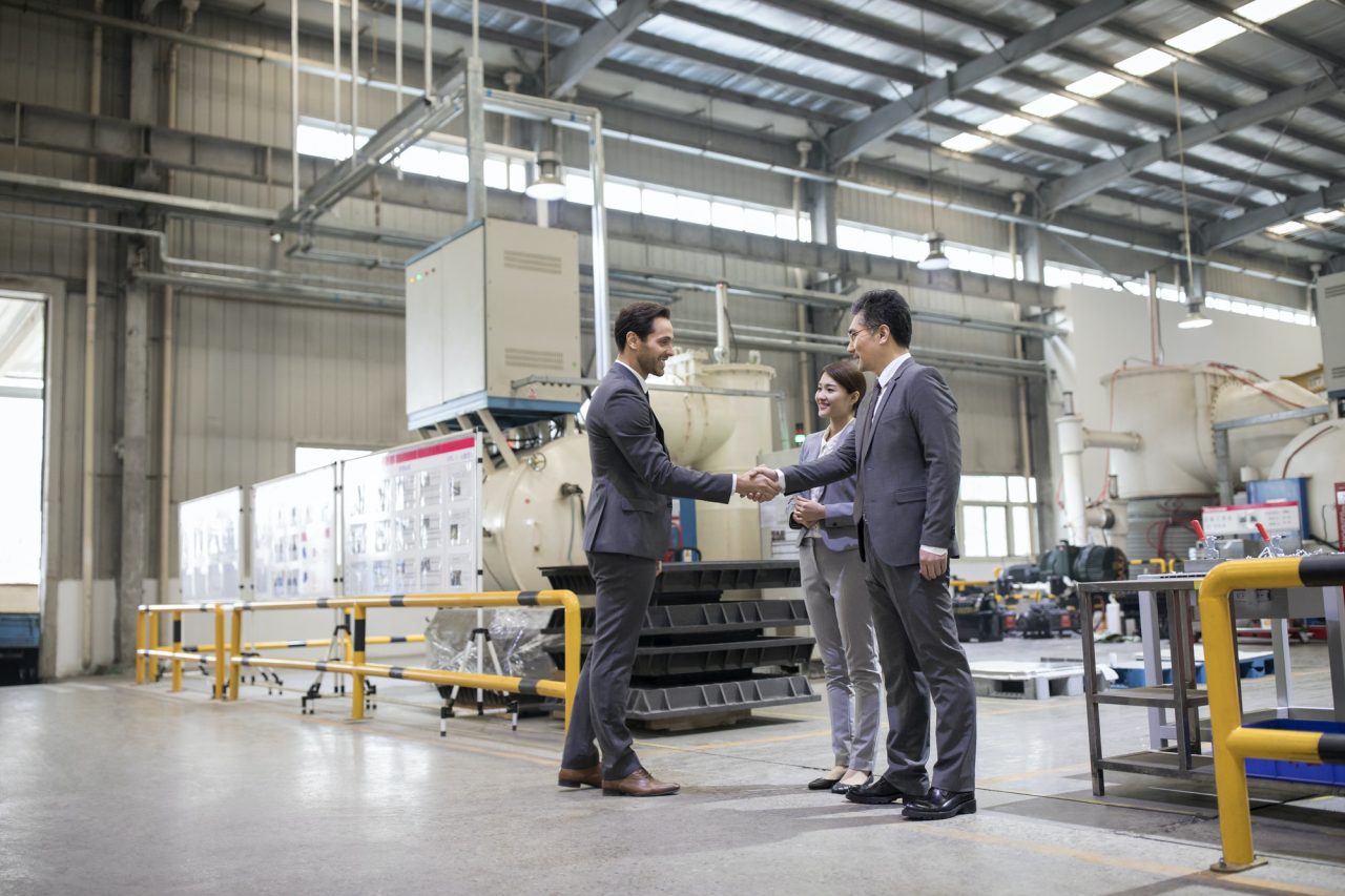Factory employees shaking hands with a man in a suit