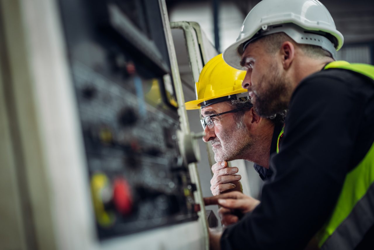 2 men in hard hats looking at the programming of a machine in a factory