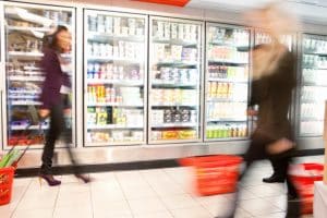 Blurred photo of shoppers in front of a commercial refrigerator